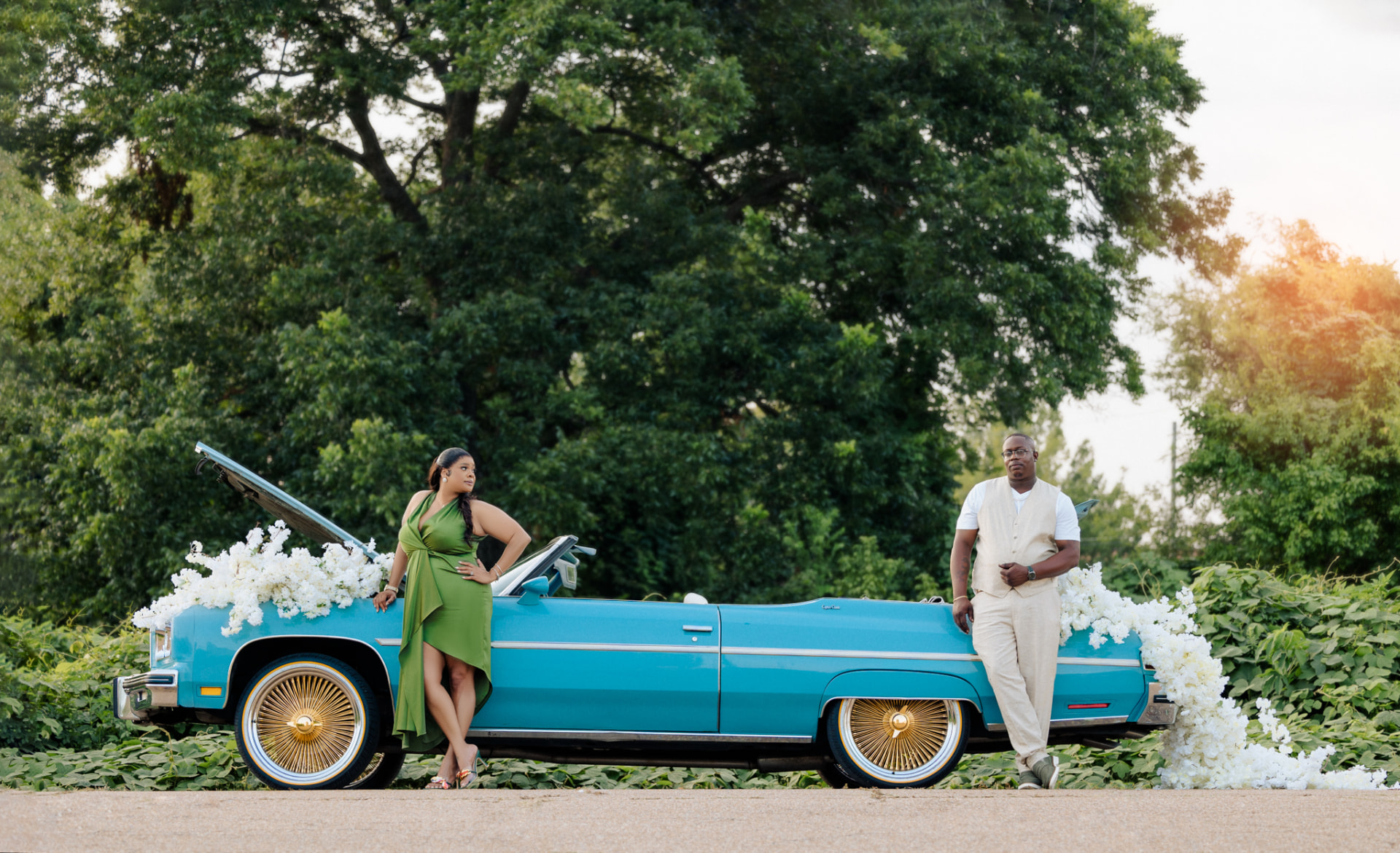 Engaged couple leaning against a vintage blue convertible decorated with white flowers