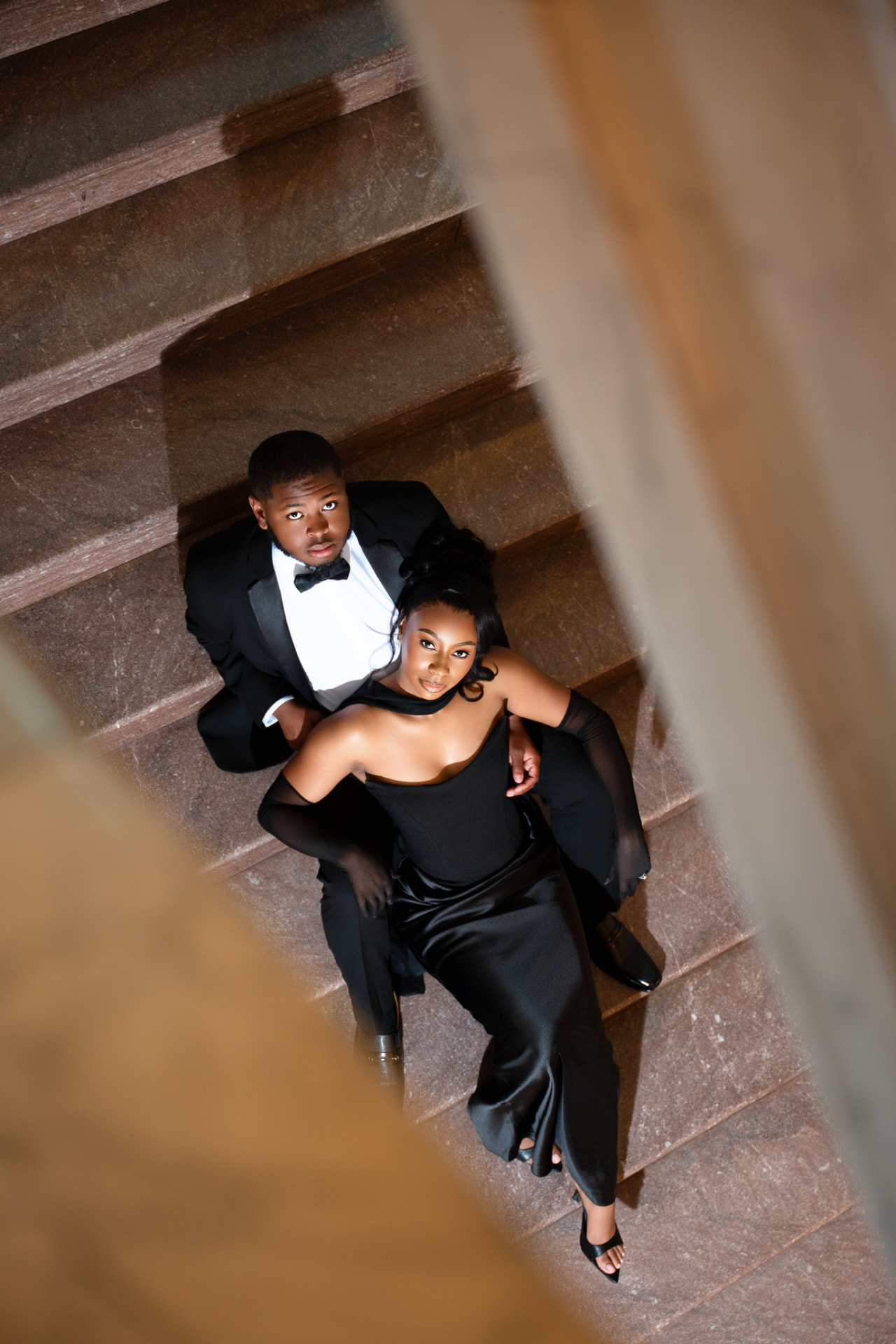 Engaged couple in black formal attire viewed from above on a staircase